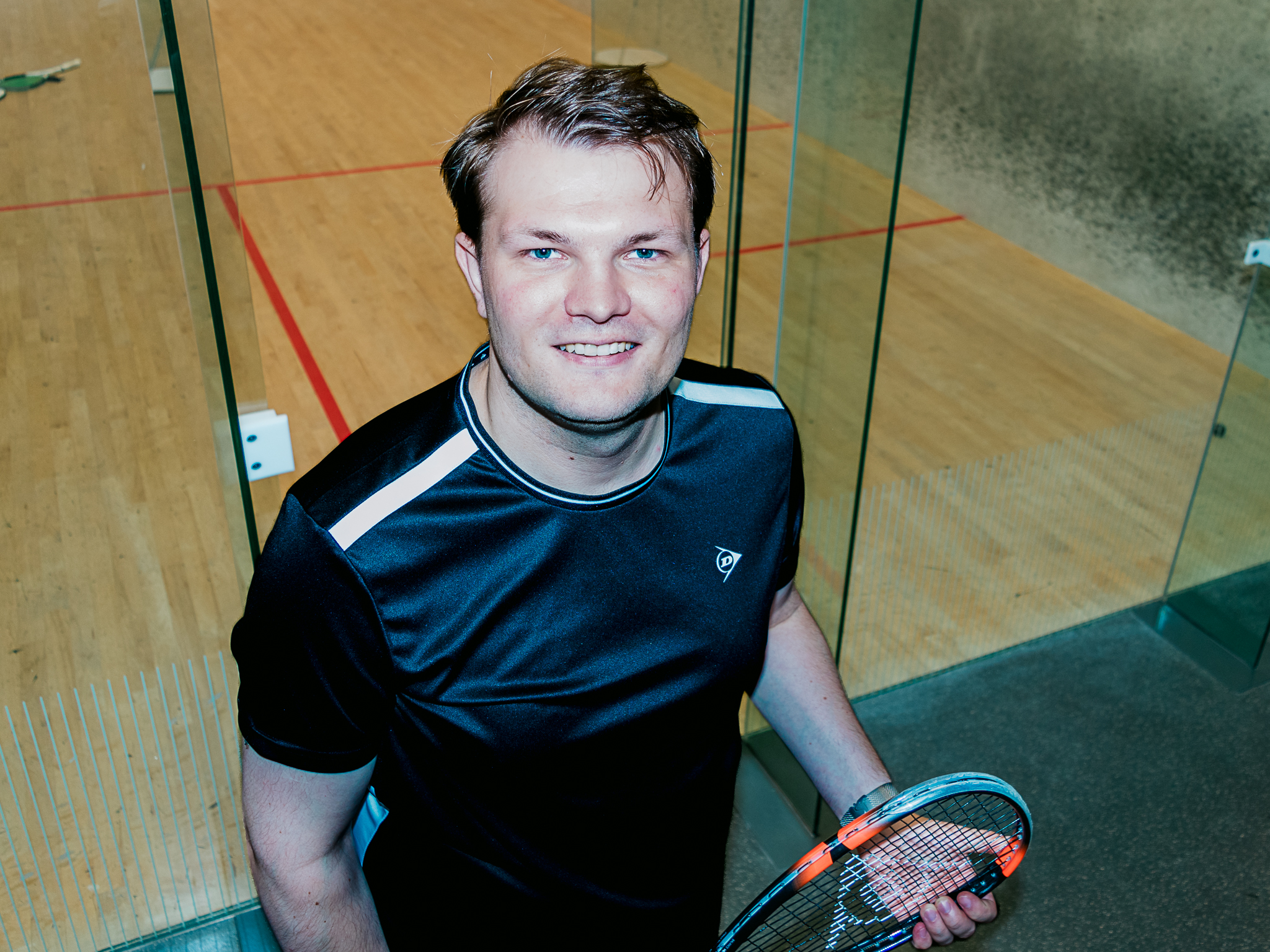 Squash player holding a racket inside a glass court