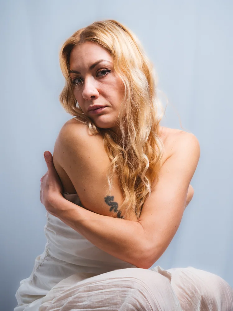 Seated studio portrait of a woman in a white wrap, resting one hand on her opposite shoulder