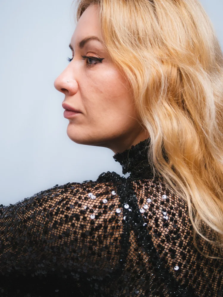 Side profile portrait of a woman with wavy blonde hair wearing a black sequined dress