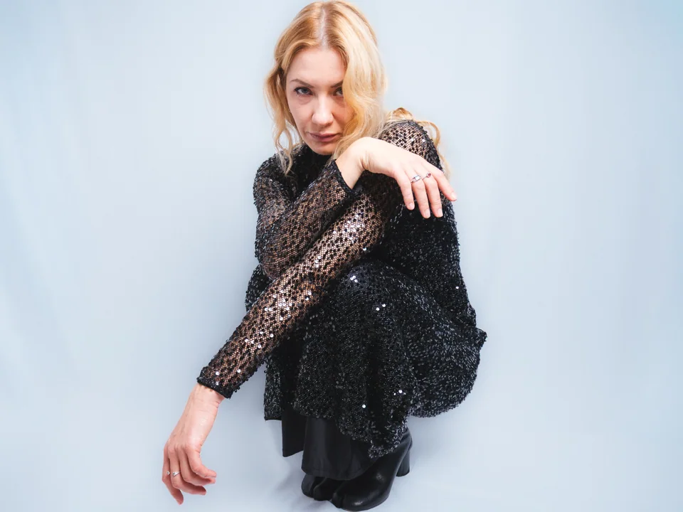 Studio portrait of a woman crouching in a black sequined dress and ankle boots