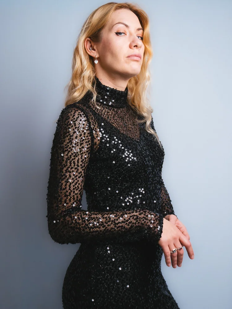 Studio portrait of a woman wearing a black sequined dress against a pale blue background