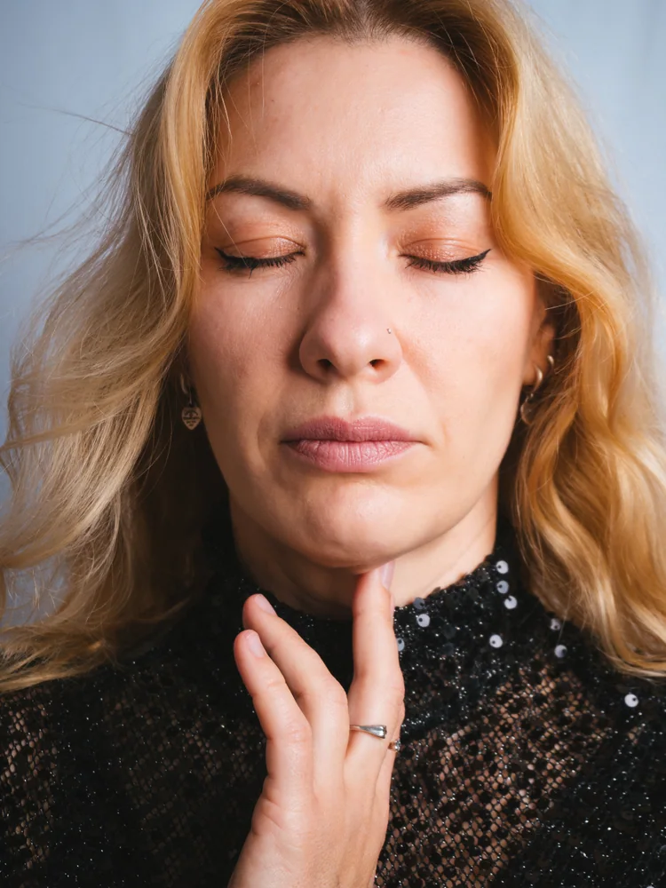 Portrait of a woman with her eyes closed and one hand touching the collar of a black sequined dress