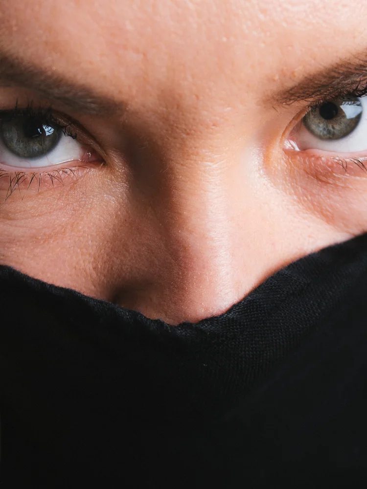 Close-up portrait of a woman looking over black fabric drawn across her face