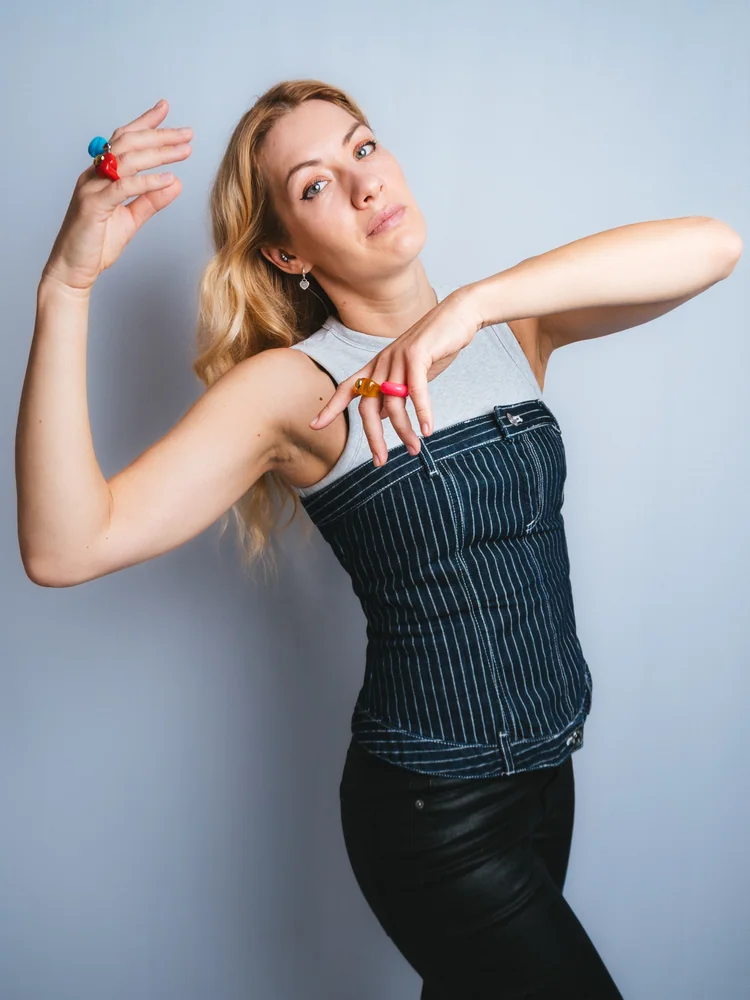 Studio portrait of a woman in a striped corset, posing with raised arms and colorful rings