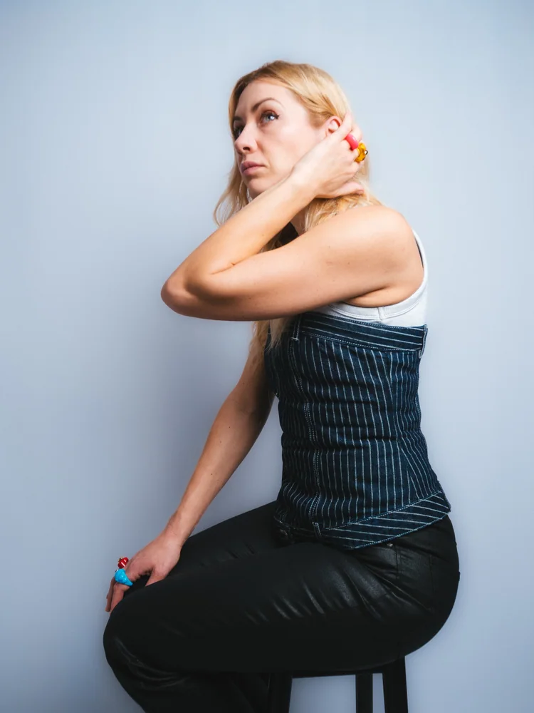 Seated studio portrait of a woman in a striped corset, turning to look over her shoulder