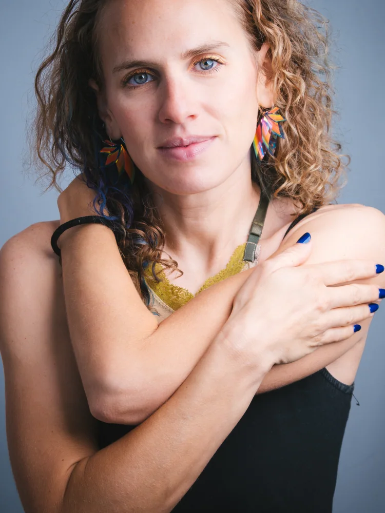 Studio portrait of a woman with curly hair and colorful earrings, her hands resting on her shoulders