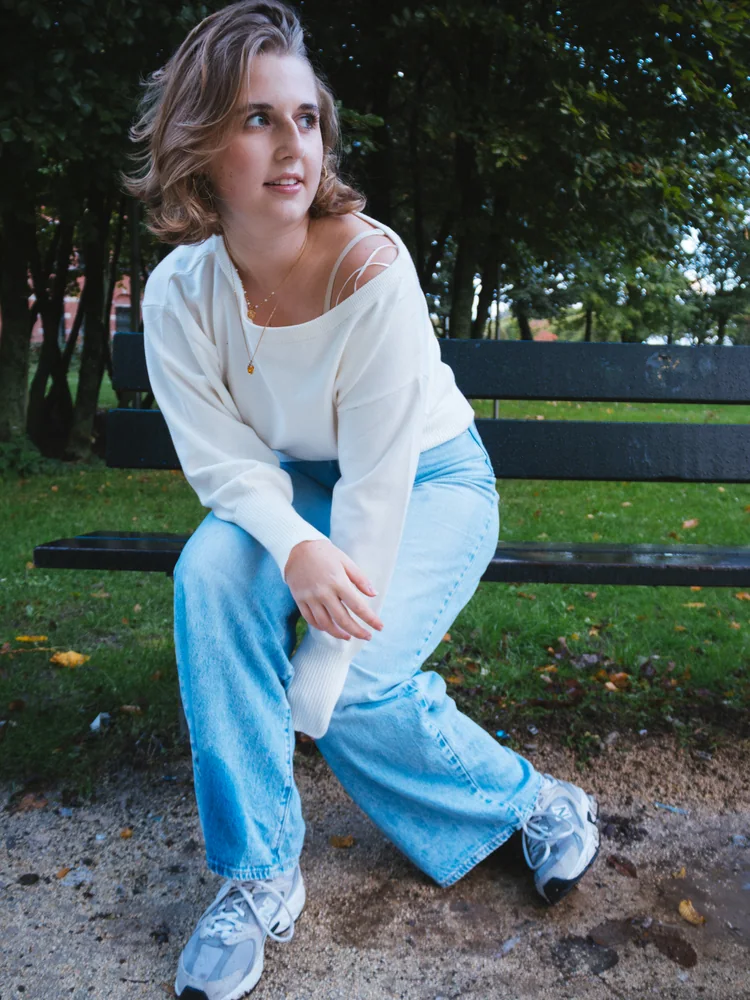 Portrait of a woman in a white sweater and blue jeans seated on a park bench