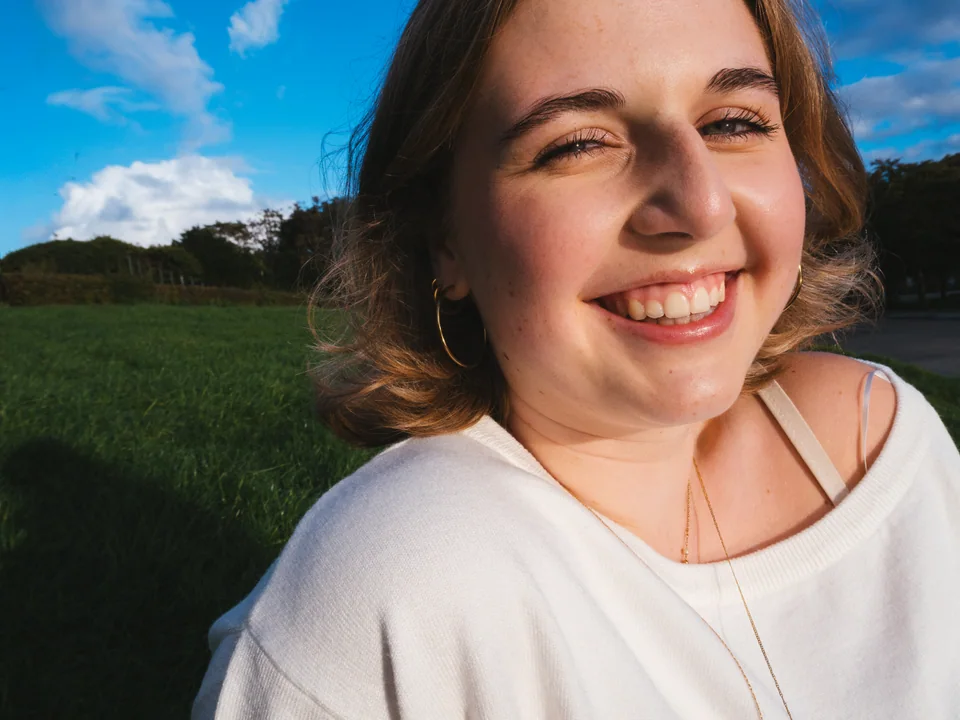 Close-up portrait of a smiling woman in a white sweater beneath a blue sky