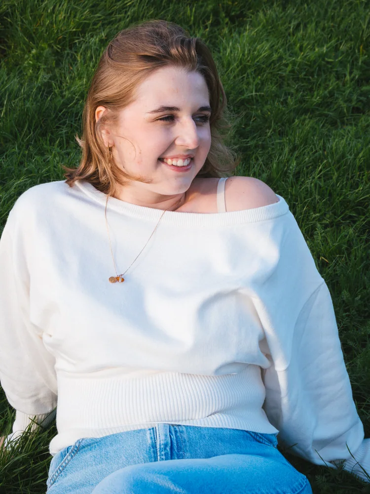 Portrait of a smiling woman in a white sweater seated on grass
