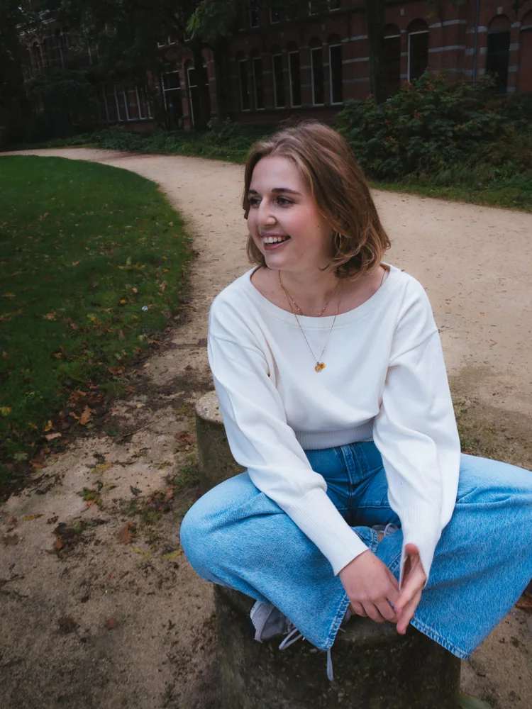 Portrait of a woman in a white sweater and blue jeans crouching in a park
