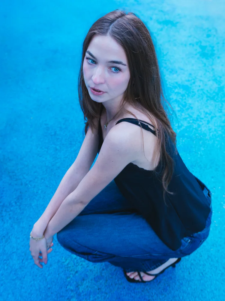 Portrait of a woman in a black dress crouching against a blue wall