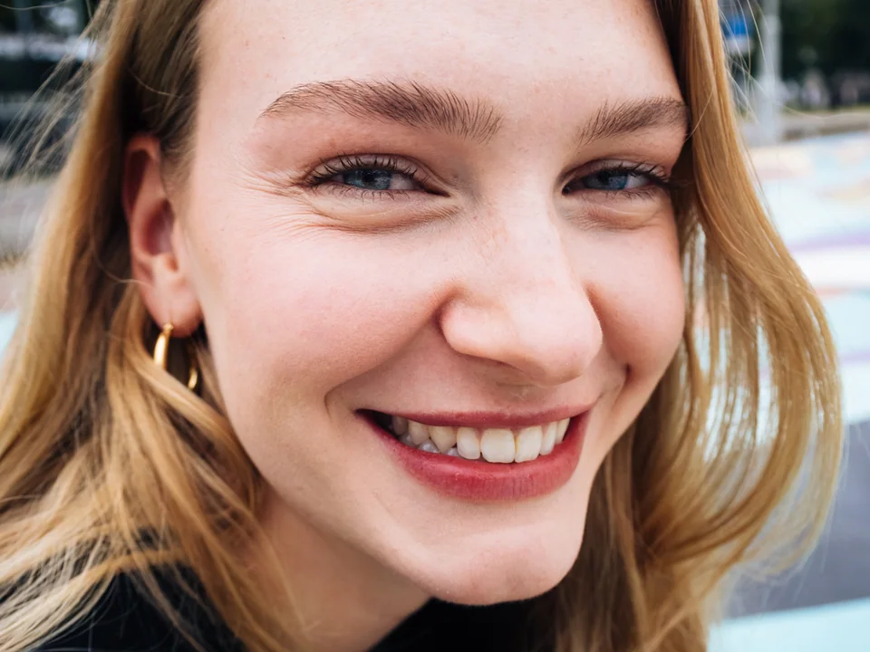 Outdoor close-up portrait of a smiling woman wearing gold earrings