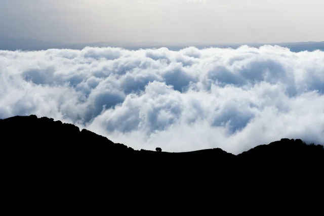 A dark mountain ridge silhouetted above a sea of clouds.