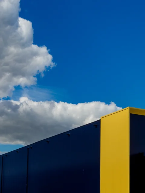 A yellow corner of a blue building beneath white clouds.