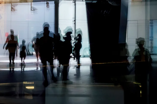 Overlapping silhouettes of people reflected in a glass interior.
