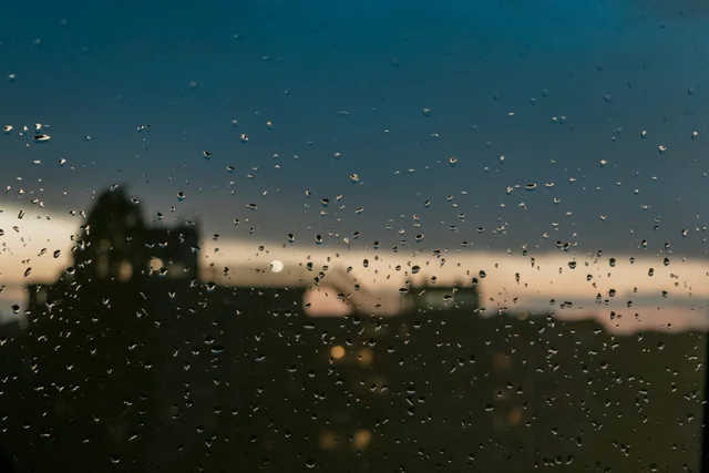 Raindrops on a window with a blurred city skyline at dusk.